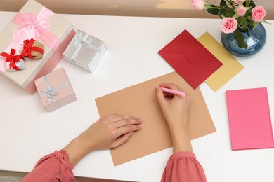 Young woman writing message in greeting card at white table, above view