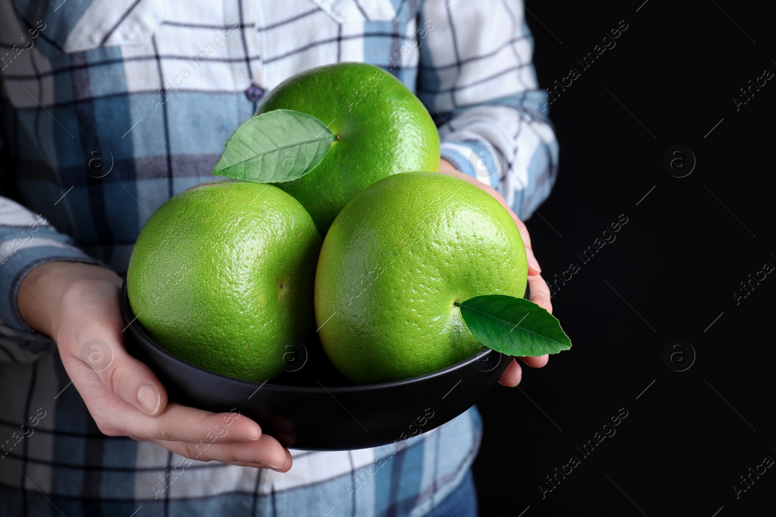 Photo of Woman holding bowl with sweetie fruits on black background, closeup