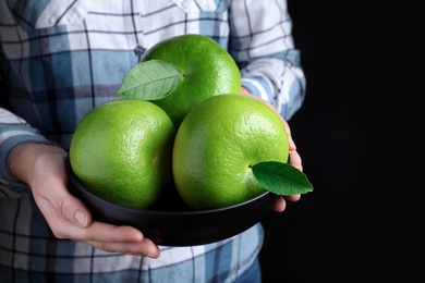 Photo of Woman holding bowl with sweetie fruits on black background, closeup