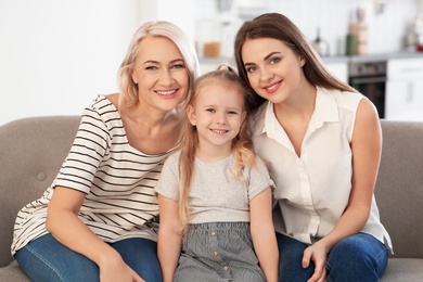 Photo of Portrait of young woman, her mature mother and daughter on sofa in living room