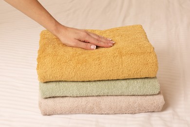 Photo of Woman touching soft towels on bed, closeup view
