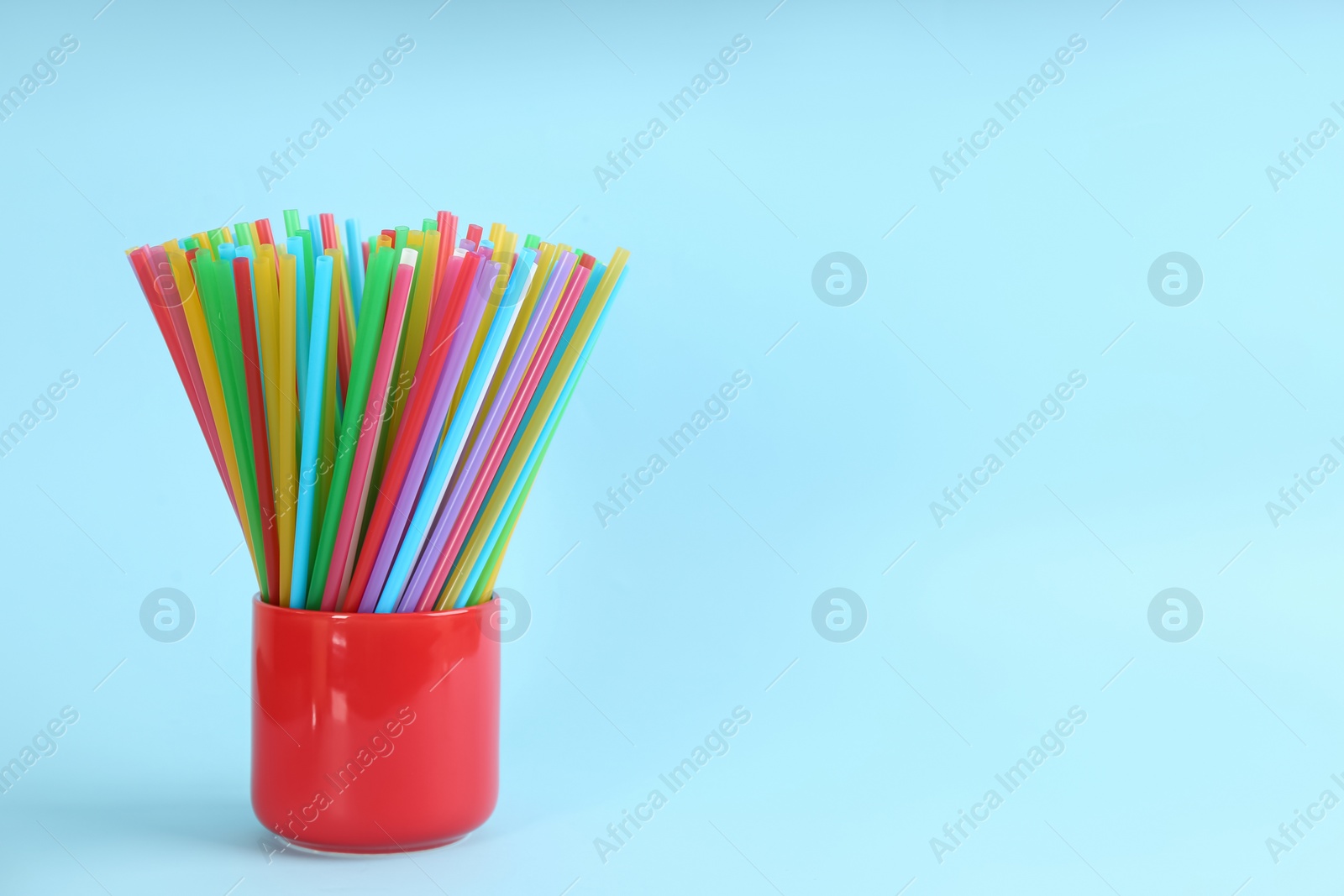 Photo of Colorful plastic drinking straws in holder on light blue background, space for text