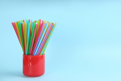 Colorful plastic drinking straws in holder on light blue background, space for text