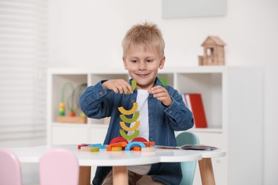 Cute little boy playing with colorful wooden pieces at white table indoors. Child's toy