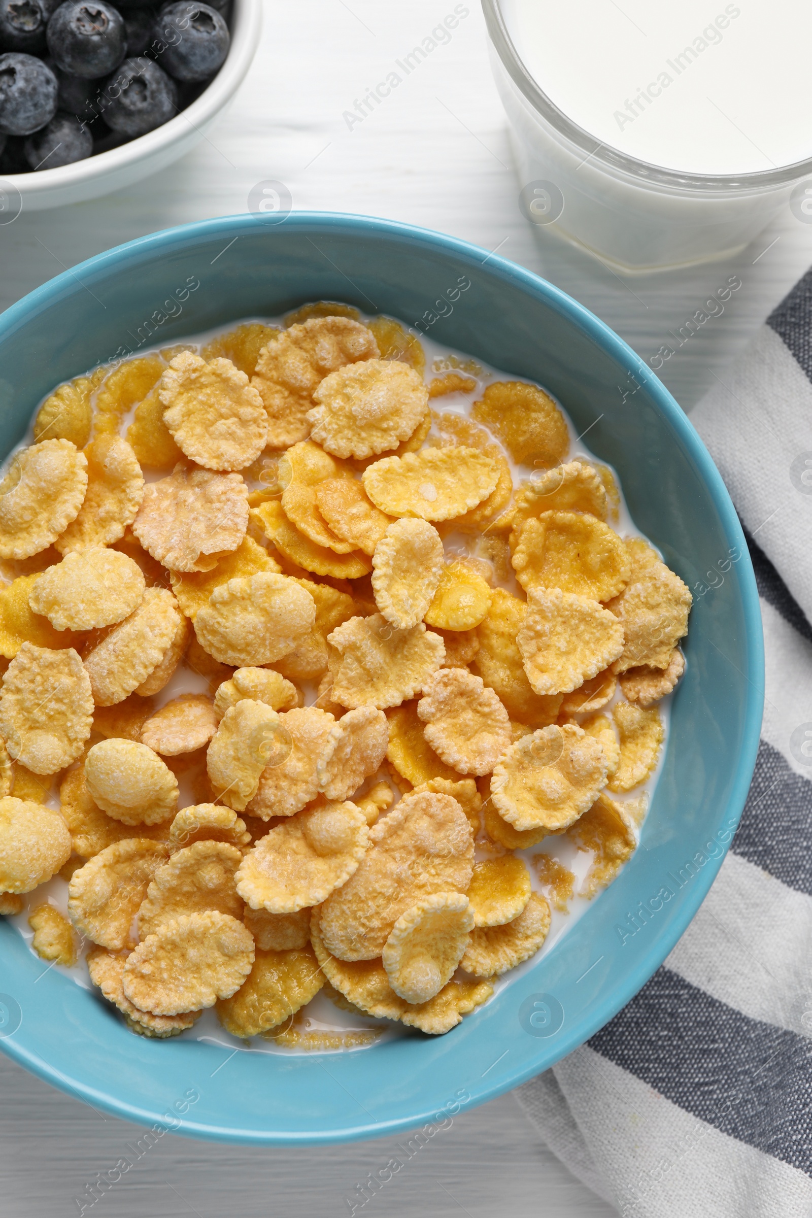 Photo of Bowl of tasty corn flakes and blueberries served for breakfast on white wooden table, flat lay