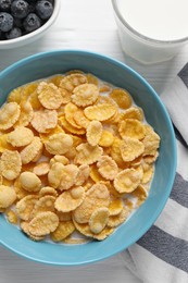 Photo of Bowl of tasty corn flakes and blueberries served for breakfast on white wooden table, flat lay