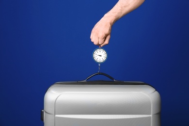 Man weighing stylish suitcase against color background, closeup