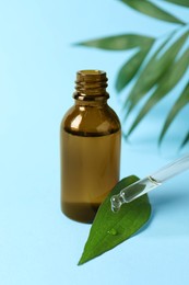 Photo of Dripping cosmetic oil from pipette into leaf on light blue background, closeup