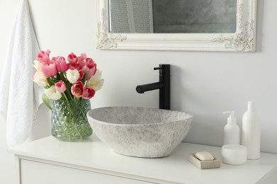 Photo of Vase with beautiful pink tulips and toiletries near sink in bathroom