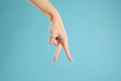 Photo of Woman imitating walk with hand on light blue background, closeup. Finger gesture