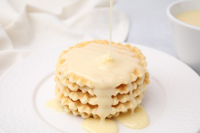 Photo of Pouring tasty condensed milk onto waffles on plate, closeup