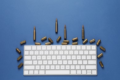 Photo of Bullets and computer keyboard on blue background, flat lay. Hybrid warfare concept