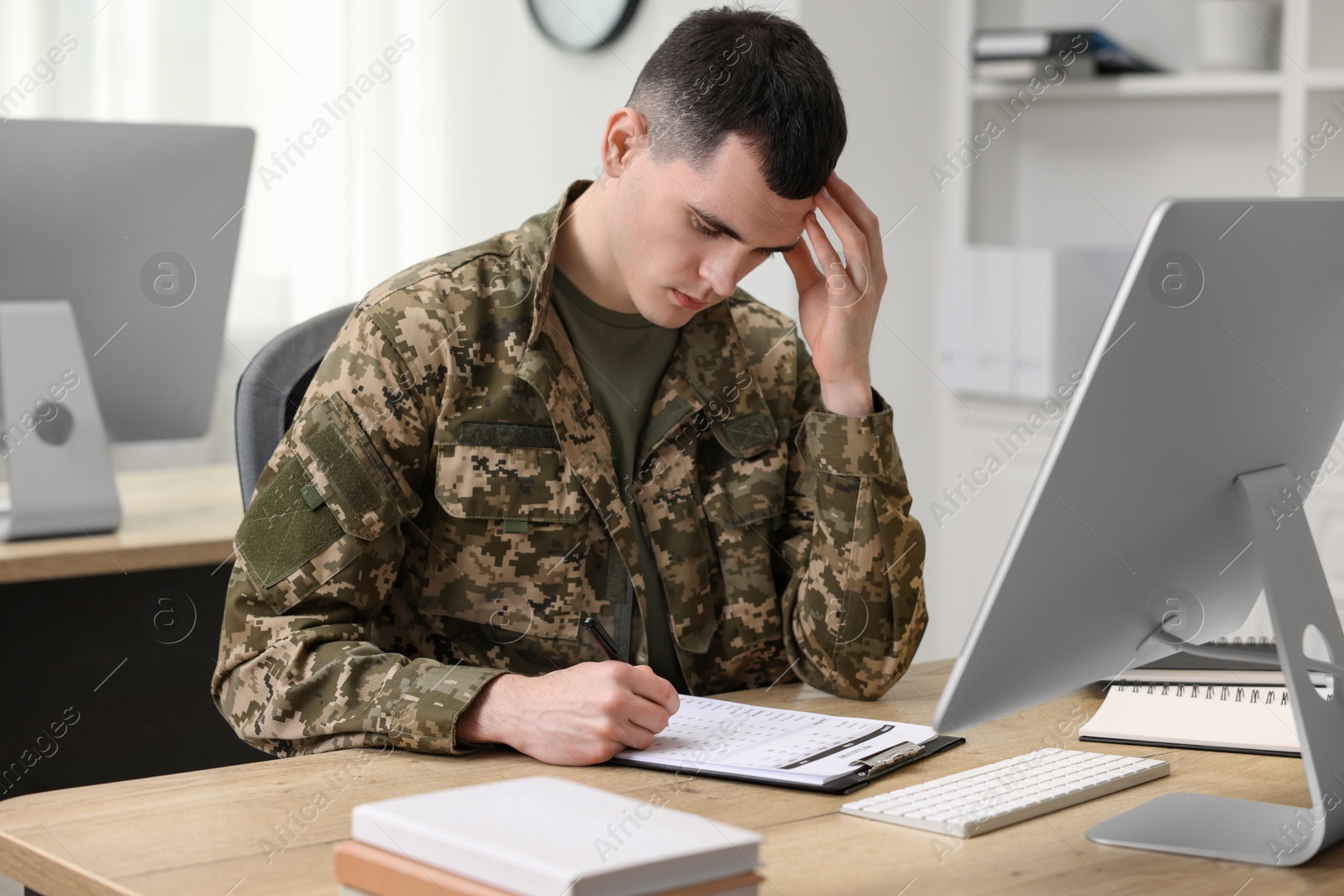 Photo of Military service. Young soldier working at wooden table in office