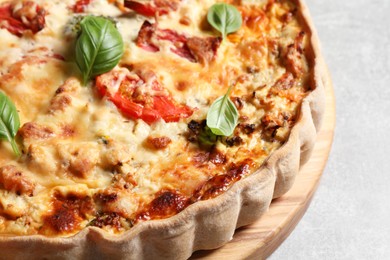 Tasty quiche with tomatoes, basil and cheese on light table, closeup