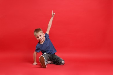 Photo of Happy little boy dancing on red background. Space for text