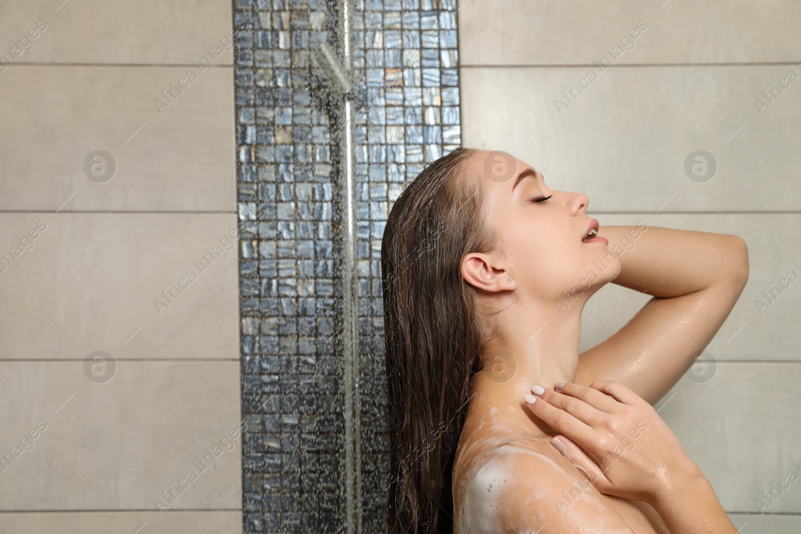 Photo of Young woman covered with soap foam taking shower in bathroom. Space for text