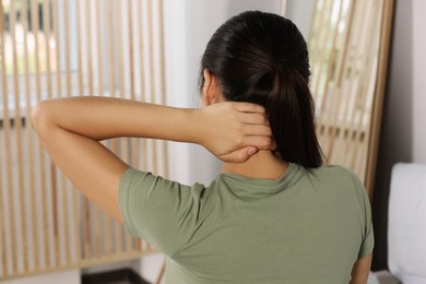 Photo of Young woman suffering from neck pain at home, back view