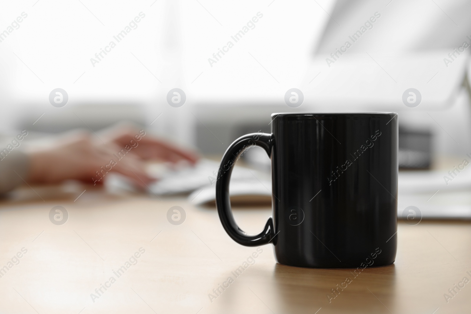 Photo of Black ceramic mug on wooden table in office, selective focus. Space for text