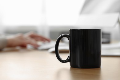 Photo of Black ceramic mug on wooden table in office, selective focus. Space for text