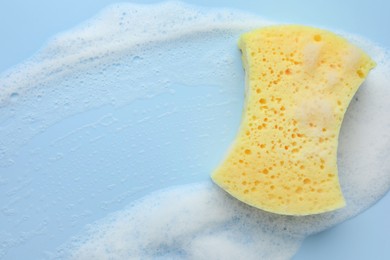 Yellow sponge with foam on light blue background, top view.