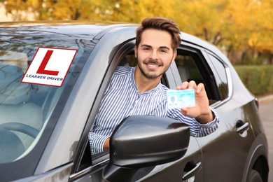 Image of Young man holding driving license in car