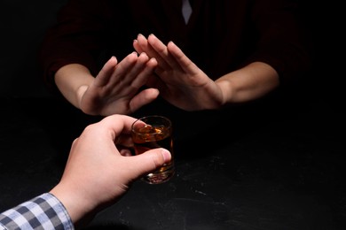 Photo of Alcohol addiction. Woman refusing glass of whiskey at dark table, closeup