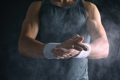 Photo of Young man applying chalk powder on hands against dark background