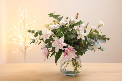 Photo of Bouquet of beautiful lily flowers in vase on wooden table against beige background