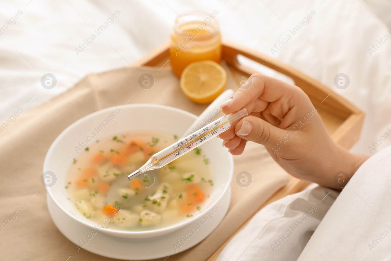 Photo of Sick woman with thermometer and bowl of fresh homemade soup to cure flu on tray in bed, closeup