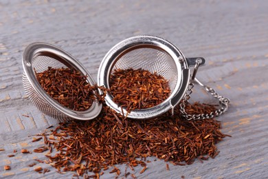 Photo of Infuser with dry rooibos leaves on grey wooden table