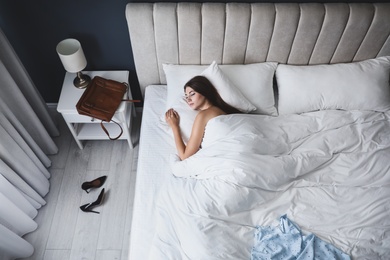 Photo of Tired woman sleeping in bed at home after work, above view