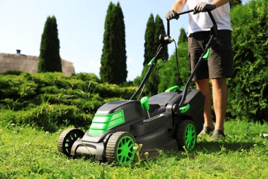 Photo of Man cutting grass with lawn mower in garden on sunny day, closeup