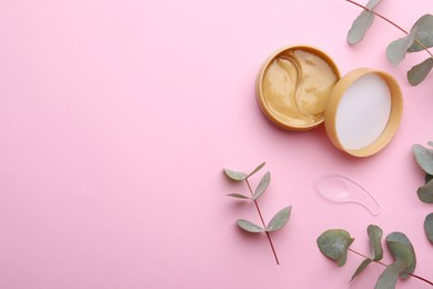 Under eye patches in jar with spatula and green twigs on light pink background, flat lay. Space for text