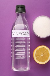 Eco friendly natural cleaners. Vinegar in bottle, cut lemon and bowl of soda on purple background, flat lay