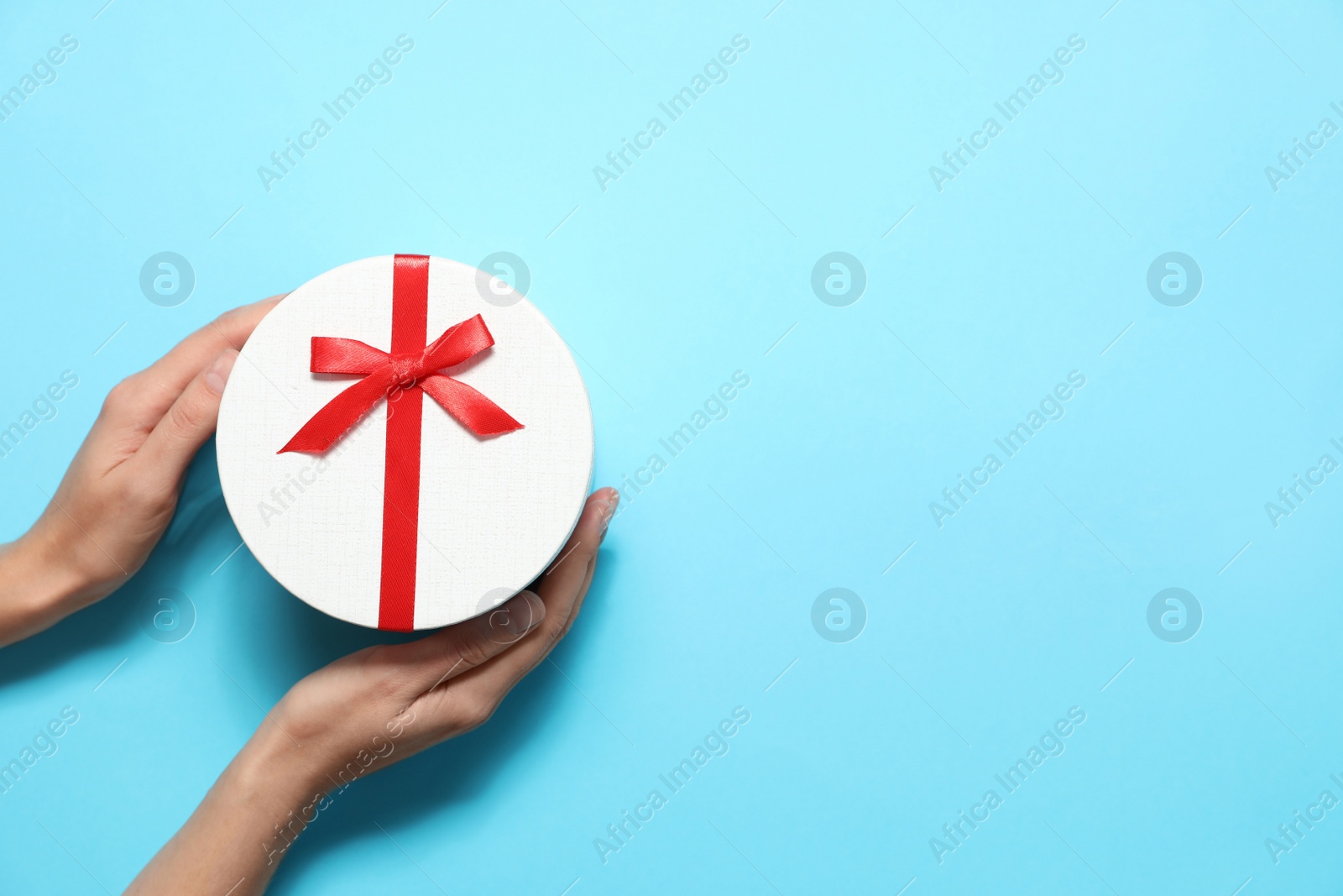 Photo of Woman holding Christmas gift on light blue background, top view. Space for text