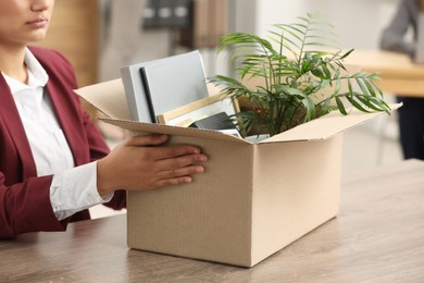 Photo of Unemployment problem. Woman with box of personal belongings at table in office, closeup