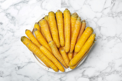 Photo of Many raw yellow carrots on white marble table, top view