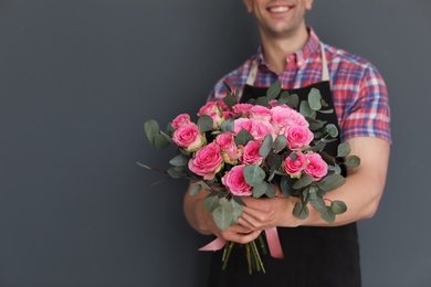 Photo of Male florist holding bouquet of beautiful flowers on dark background