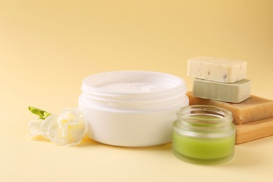 Photo of Moisturizing cream in open jars, soap bars and freesia flower on beige background. Body care products