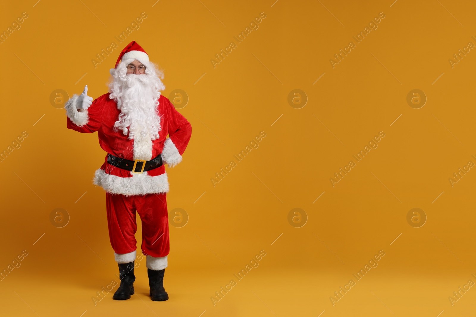 Photo of Merry Christmas. Santa Claus showing thumbs up on orange background, space for text