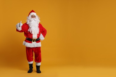 Photo of Merry Christmas. Santa Claus showing thumbs up on orange background, space for text
