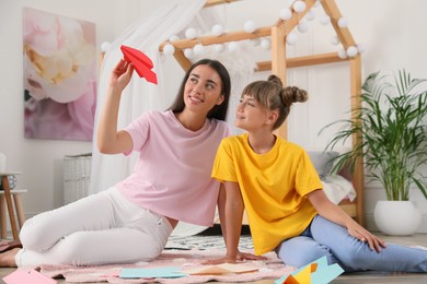 Photo of Happy mother and daughter playing with paper plane on floor in room