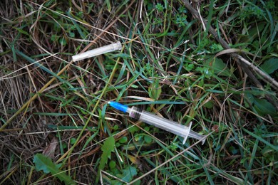 Photo of Empty syringe on green grass outdoors, flat lay