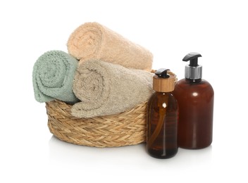 Photo of Soft towels in wicker basket and bottles of cosmetic products on white background