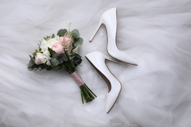Pair of wedding high heel shoes and beautiful bouquet on white veil, flat lay