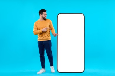 Man pointing at huge mobile phone with empty screen on light blue background. Mockup for design