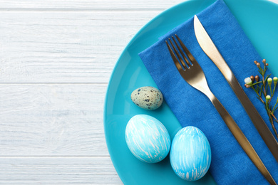 Festive Easter table setting with eggs and floral decoration on wooden background, flat lay