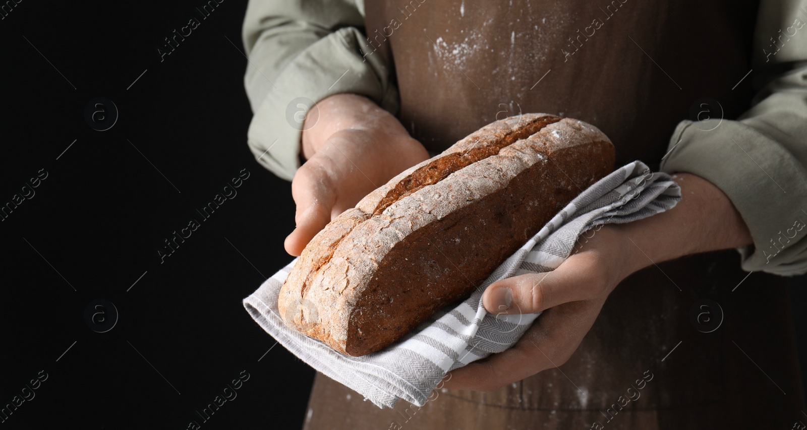 Photo of Woman holding freshly baked bread on black background, closeup. Space for text