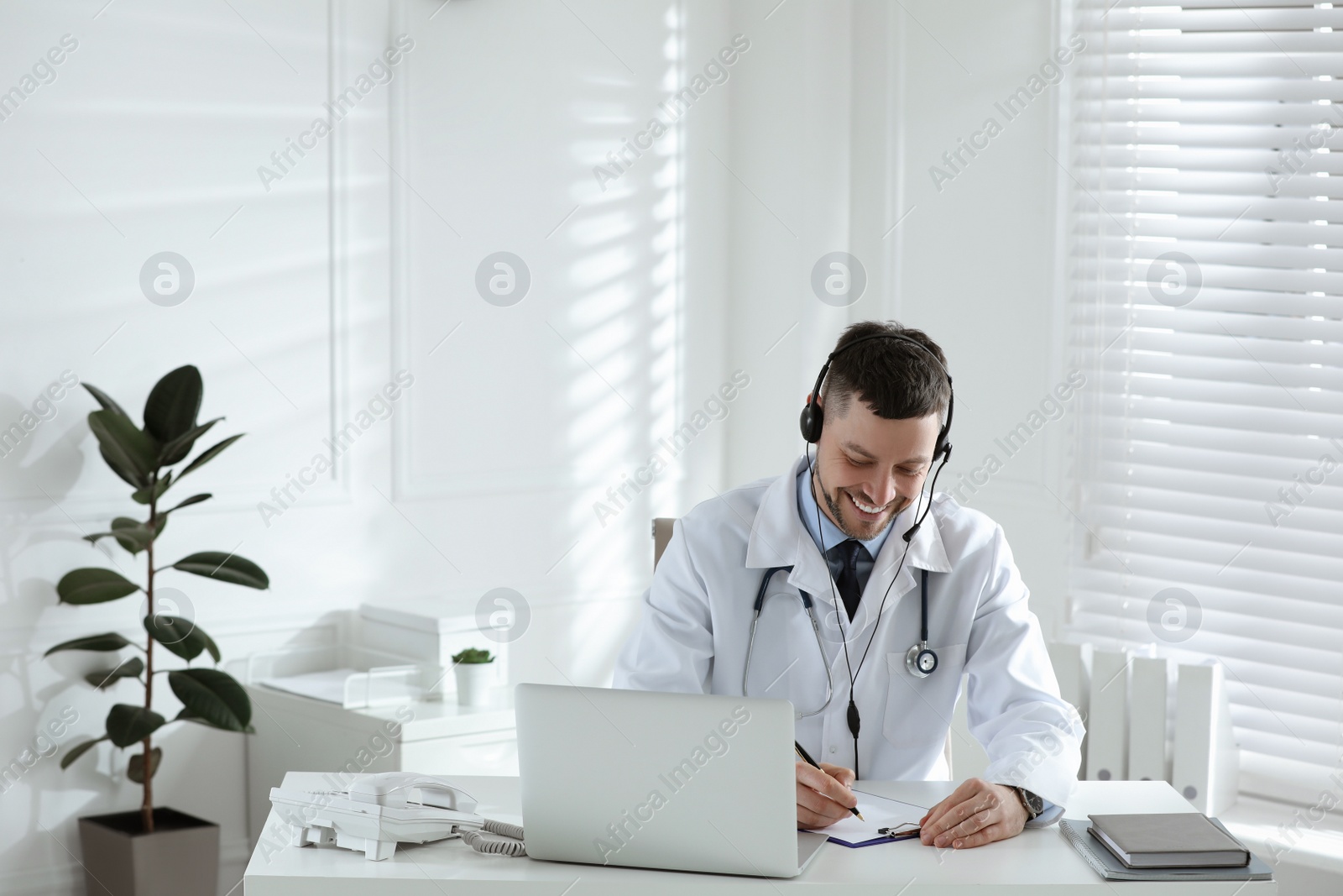 Photo of Doctor with headset consulting patient online at desk in clinic. Health service hotline