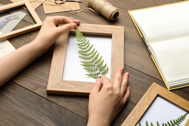 Photo of Woman making beautiful herbarium with pressed dried fern leaf at wooden table, closeup